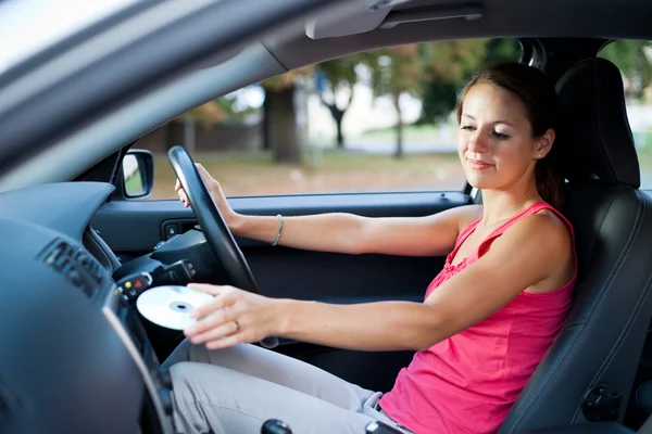 Jonge vrouwelijke bestuurder afspelen van muziek in de auto (het veranderen van cd 's) — Stockfoto