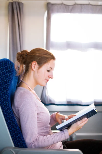Mujer joven leyendo un libro mientras está en un tren — Foto de Stock