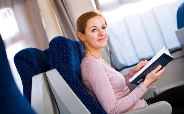 Mujer joven leyendo un libro mientras está en un tren — Foto de Stock