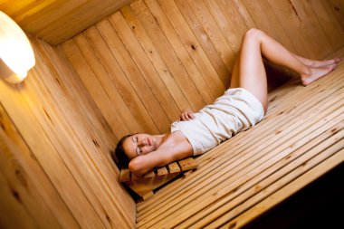 Genç bir kadın saunada dinleniyor.