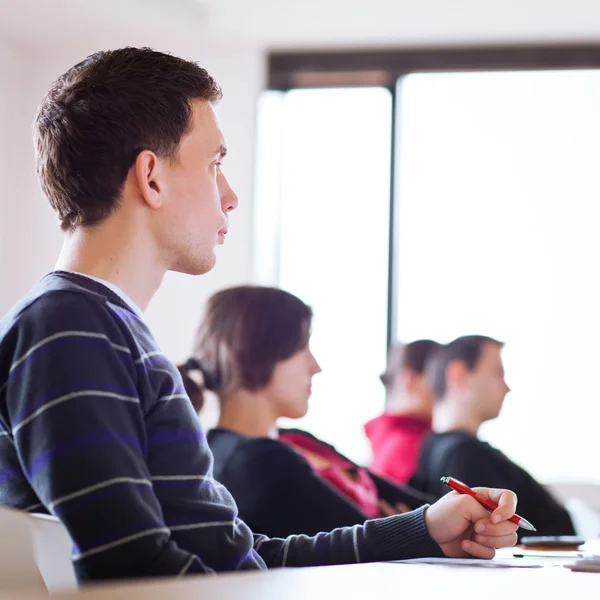 Ung, stilig hane högskolestudent som sitter i ett klassrum — Stockfoto