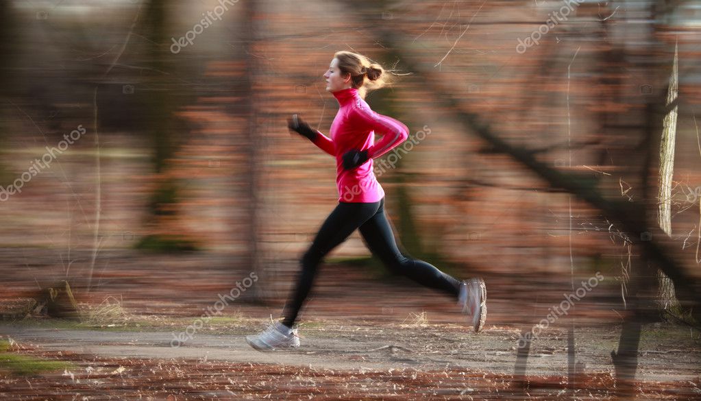 Young woman running outdoors in a city park on a cold fall - Stock