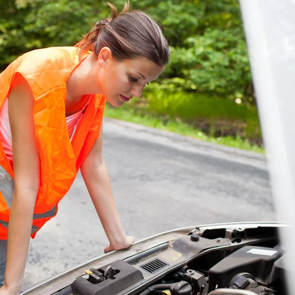 Молодая женщина-водитель наклоняется над двигателем своей сломанной машины — стоковое фото