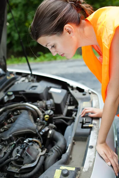 Молодая женщина-водитель наклоняется над двигателем своей сломанной машины — стоковое фото