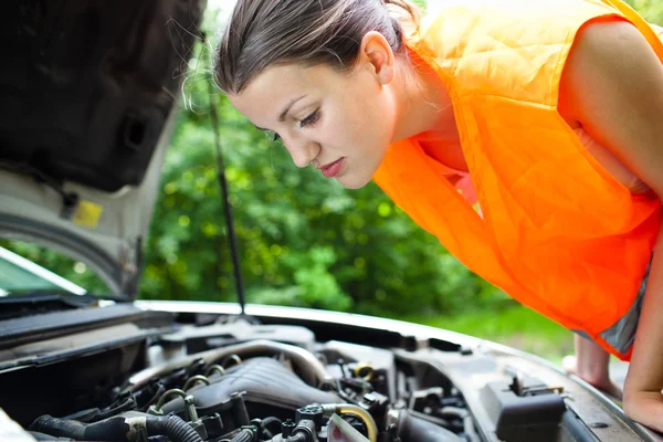 Молода жінка-водій нахиляється над двигуном свого зламаного автомобіля — стокове фото