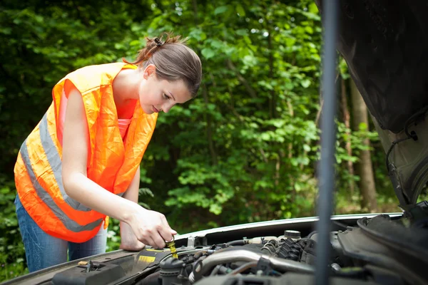 Young female driver bending over the engine of her broken down car — Stock Photo, Image
