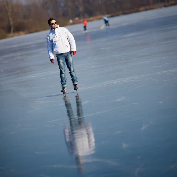 Bello giovane uomo pattinaggio su ghiaccio all'aperto su uno stagno — Foto Stock