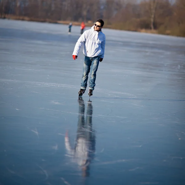 Guapo joven patinaje sobre hielo al aire libre en un estanque — Foto de Stock