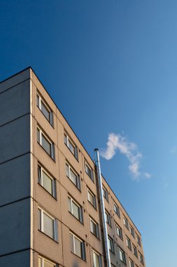 Smoke/flue gases going out of a chimney by an apartment building clipart