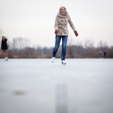 Young woman ice skating outdoors on a pond clipart