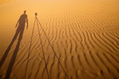 Shadow of a photographer standing next to his tripod cast clipart