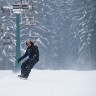 Young man snowboarding down a slope on a snowy winter day clipart