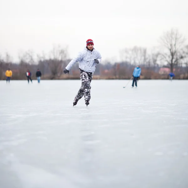 Guapo joven patinaje sobre hielo al aire libre en un estanque en un wi nublado — Foto de Stock