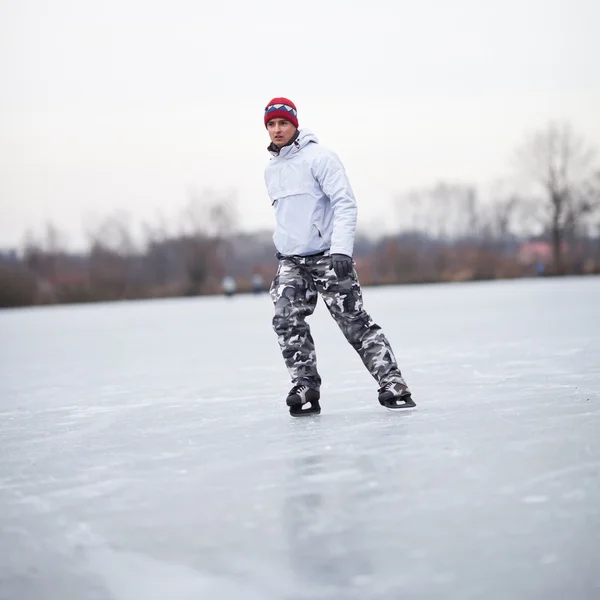 Bello giovane uomo pattinare sul ghiaccio all'aperto su uno stagno su un wi nuvoloso — Foto Stock