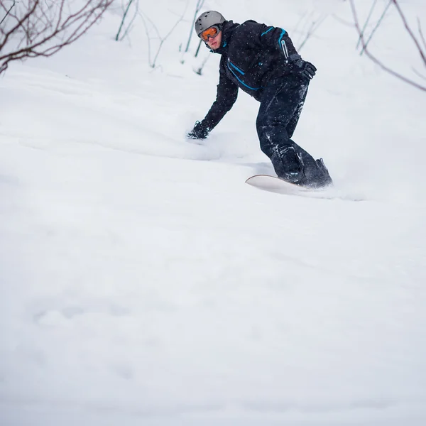 Νεαρός άνδρας snowboarding κάτω από μια κλίση σε μια χιονώδη χειμερινή ημέρα — Φωτογραφία Αρχείου