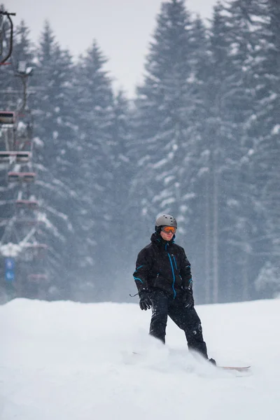 Νεαρός άνδρας snowboarding κάτω από μια κλίση σε μια χιονώδη χειμερινή ημέρα — Φωτογραφία Αρχείου