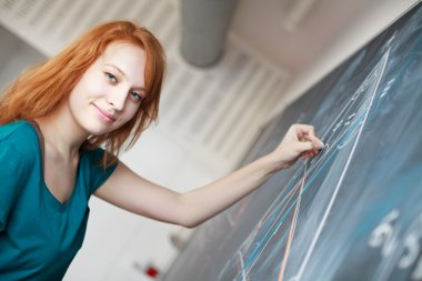 Pretty young college student writing on the chalkboard/blackboar clipart