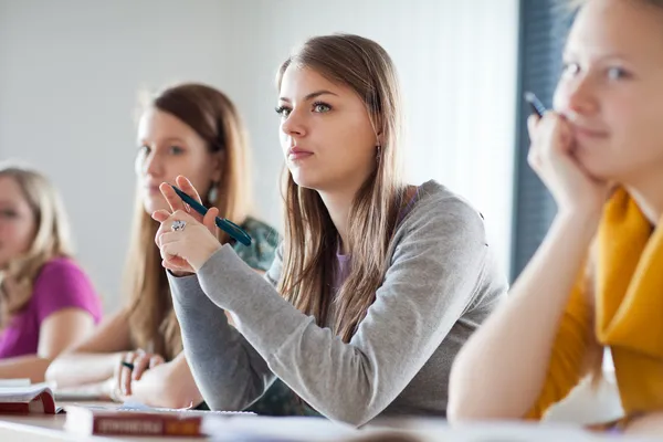 Ung ganska kvinnliga collegestudent sitter i ett klassrum fullt — Stockfoto