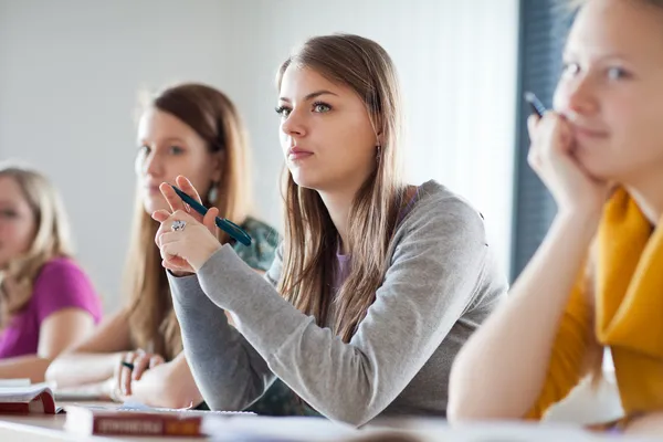 Joven bonita estudiante universitaria sentada en un aula llena — Foto de Stock