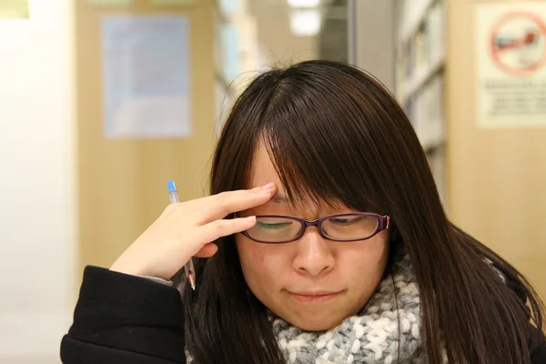 Mulher asiática pensando e estudando na biblioteca — Fotografia de Stock
