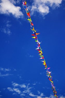 Multi colored party flags on a line on a background of blue sky clipart