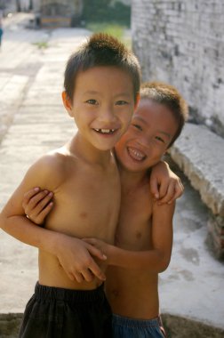 Two young Chinese boys smiling in a village clipart