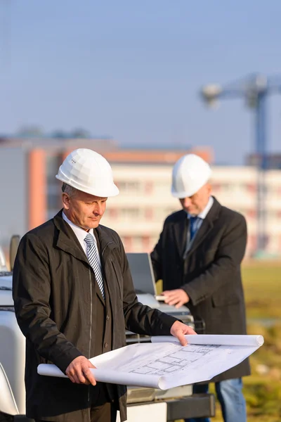 Two architects at construction site review plans — Stock Photo, Image