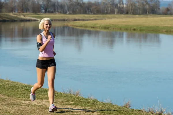 Junge Frau joggt am sonnigen Flussufer — Stockfoto
