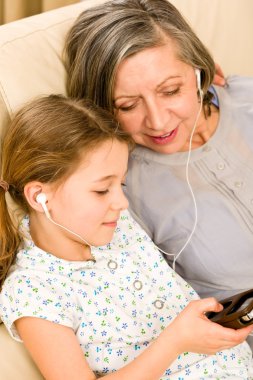 Grandmother and young girl listen music together clipart