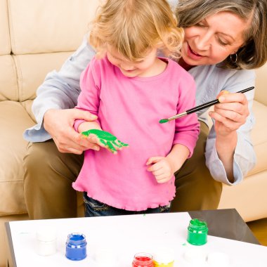 Little girl with grandmother play paint handprints clipart