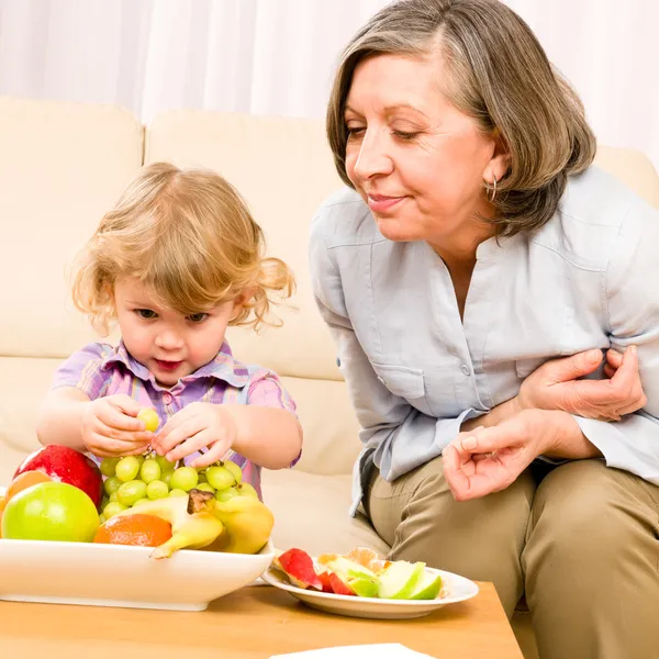 Nagymama és unokája eszik gyümölcsöt otthon — Stock Fotó