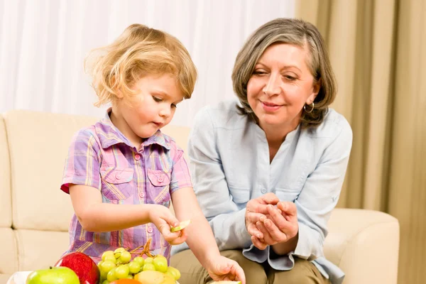Grandmother with granddaughter eat fruit at home — Stock Photo, Image