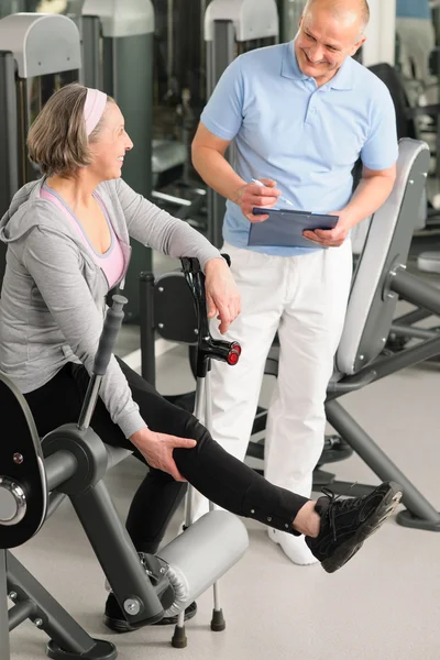 Sjukgymnast hjälpa aktiv senior kvinna på gym — Stockfoto