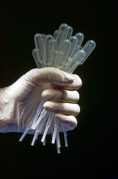 Hand in white gloves holding many pipettes — Stock Photo, Image
