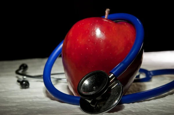 Увеличенное яблоко в окружении синего медицинского стетоскопа — стоковое фото