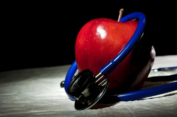 Red apple surrounded by blue medical stethoscope — Stock Photo, Image