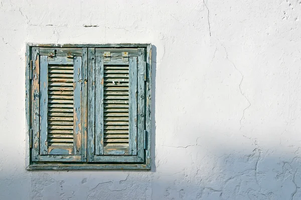 Het oude venster met blauwe luiken op een witte muur — Stockfoto