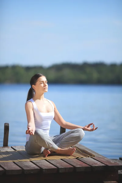 Hermosa joven entrenando yoga cerca de un lago —  Fotos de Stock