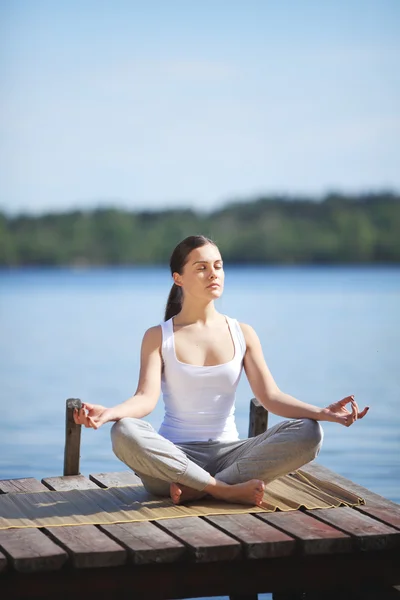 Hermosa joven entrenando yoga cerca de un lago —  Fotos de Stock