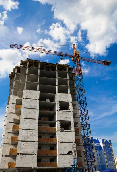 Crane and the house under construction against the blue sky with white clouds in the summer sunny day — Stock Photo, Image