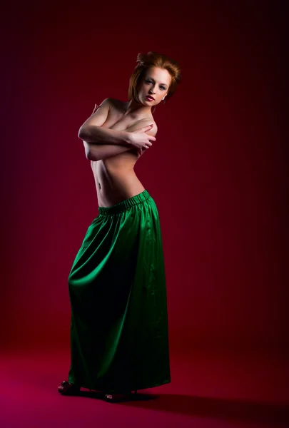 Skönhet kvinna poserar på rött i grön klänning — Stockfoto