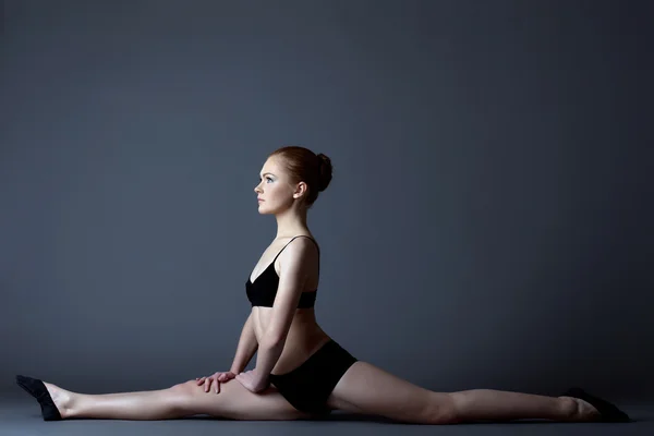 Beauté fille en noir gymnaste costume assis sur split — Photo