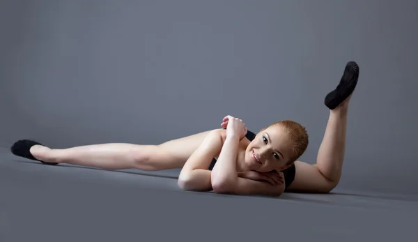 Legrační gymnastka dívka v černém top položit na zem — Stock fotografie