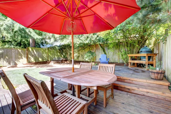 На заднем дворе большая палуба с красным зонтиком и стульями . — стоковое фото