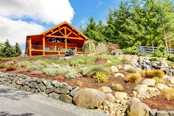 Log cabine casa na colina com cachoeira e flores . — Fotografia de Stock