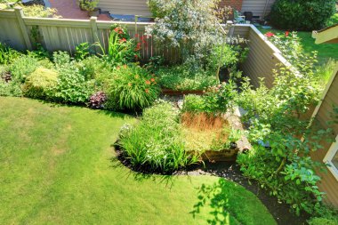 Fenced back yard corner with flowers and shrubs landscape. clipart