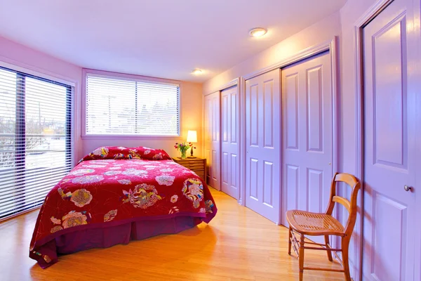 Фиолетовая спальня с розово-красной кроватью и цветами — стоковое фото