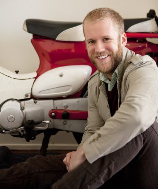 man zit naast de rode en witte fiets scooter.