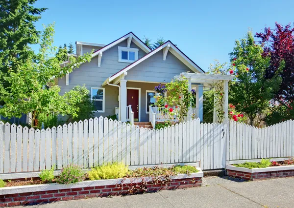Kleine grijze ambachtsman stijl huis achter witte hek. — Stockfoto