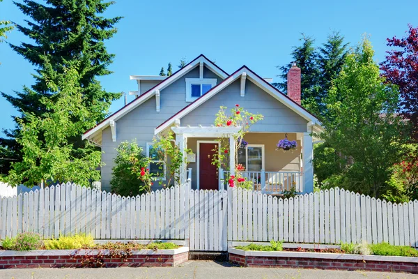 Pequeña casa linda gris con valla blanca y puertas . — Foto de Stock